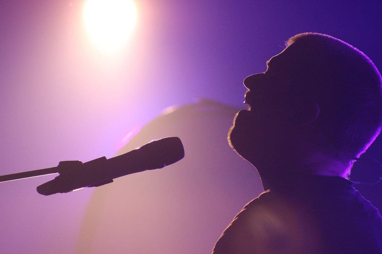 A singer's silhouette at a microphone under purple stage light.