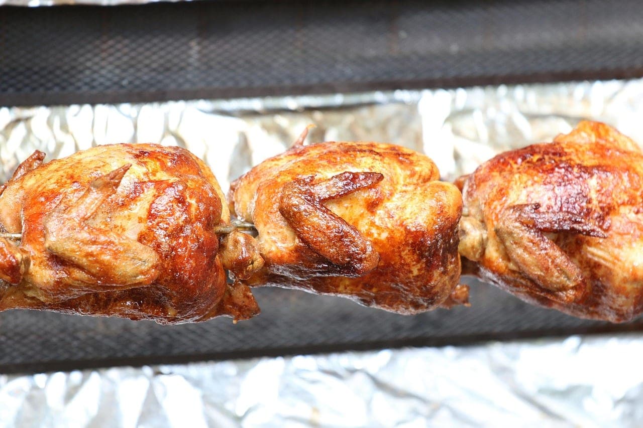 Three whole chickens browning on the spit, lined up over the heat.