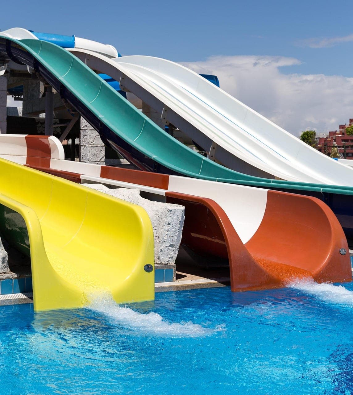 Four coloured slides emptying into the pool under a blue sky.