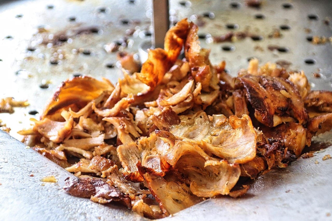 Sliced, golden shawarma meat piled on a stainless steel plate.