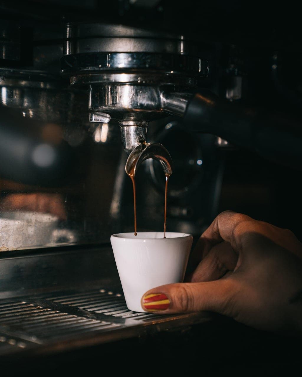 A shot of espresso runs from the machine into a small white cup at the counter.