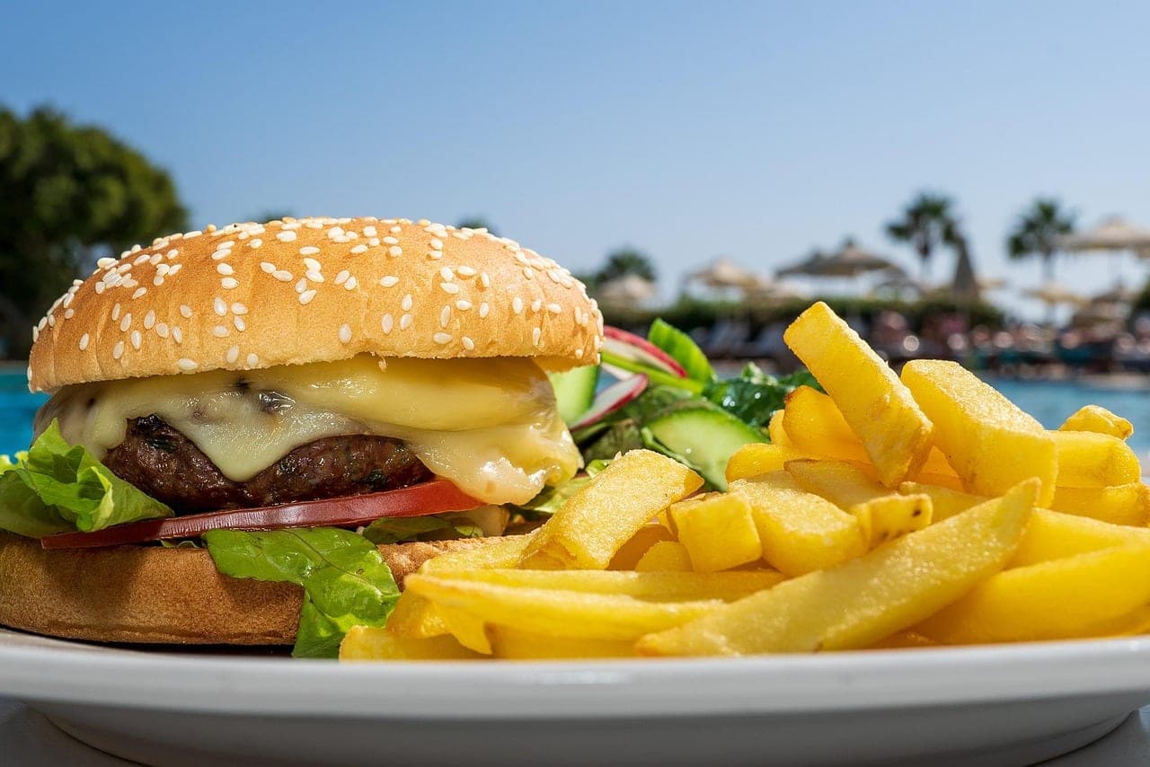 A cheeseburger with melted cheese and a serving of chips, on an outdoor table.