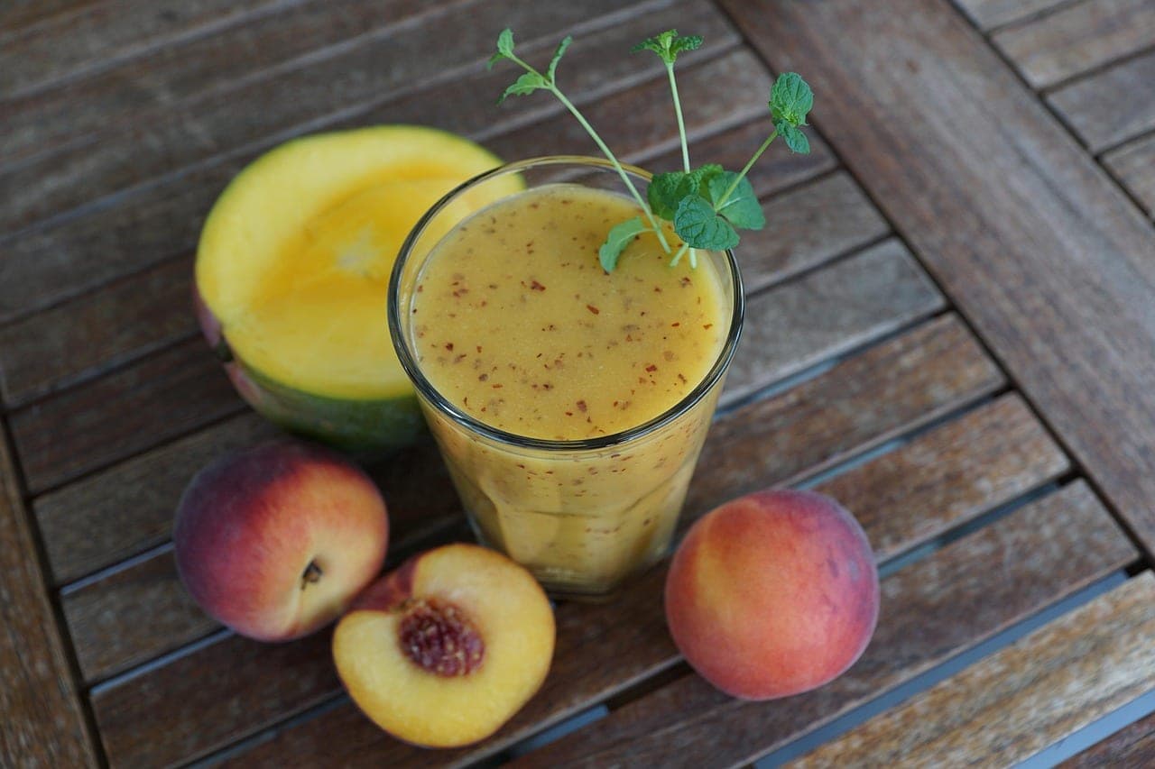 A glass of mango and peach juice with mint, on a wooden terrace table.