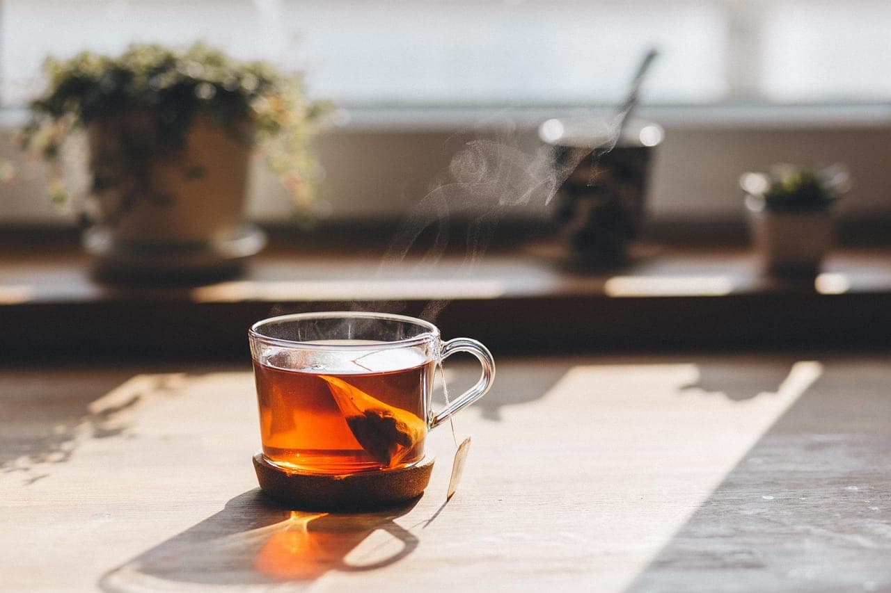 A steaming glass of hot tea standing on a wooden table.