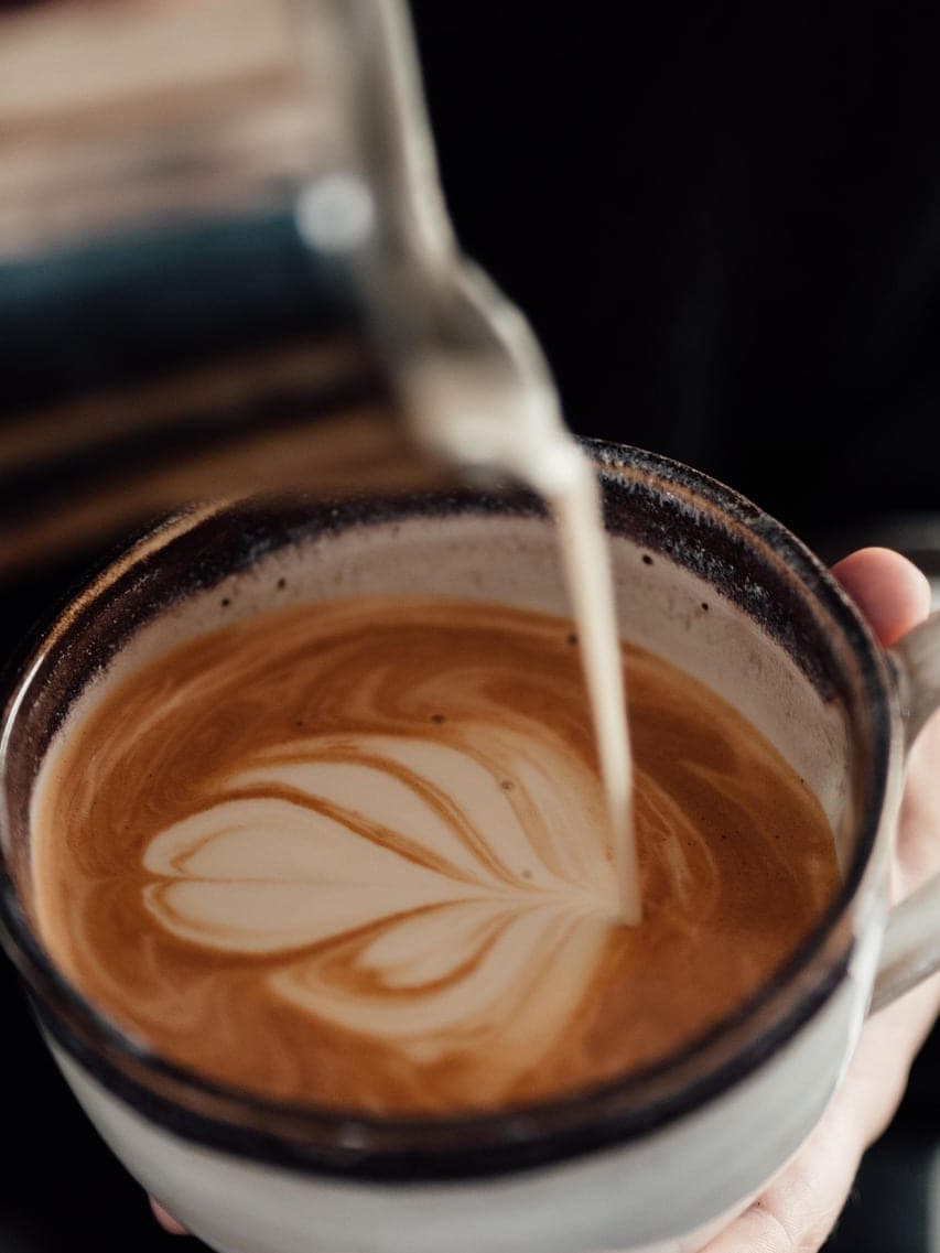 Milk poured into a cappuccino, drawing a leaf in the foam.