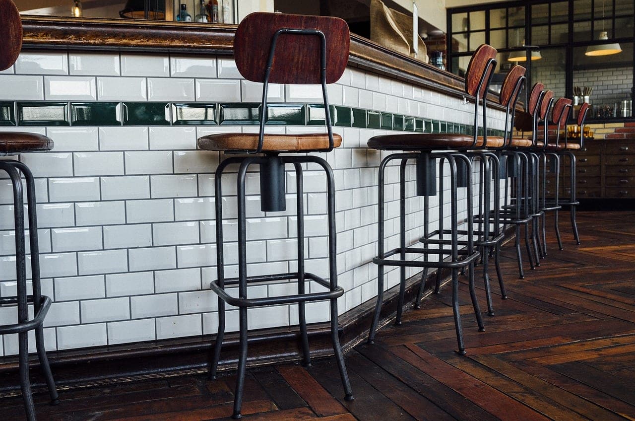 A row of high stools along a white-tiled bar counter.