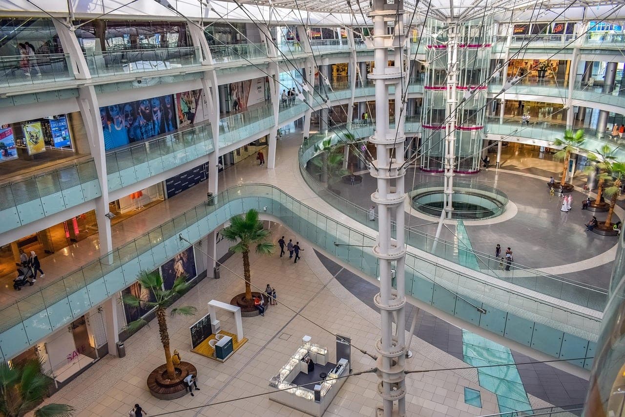 The atrium of a modern shopping mall: several levels, potted palms and a pool.