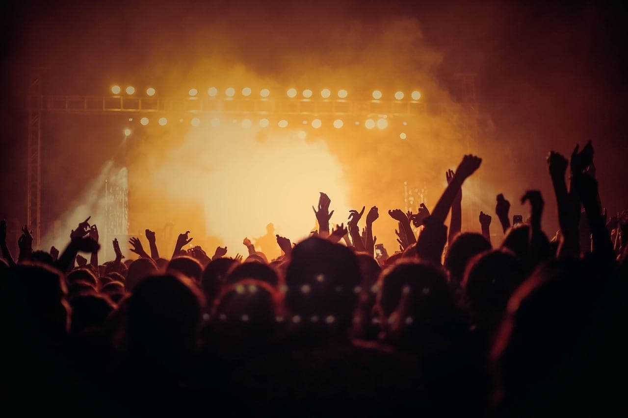A crowd in silhouette, arms raised in front of a stage flooded with orange light.