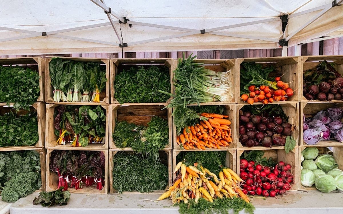 Vegetables sorted into wooden crates, under the awning