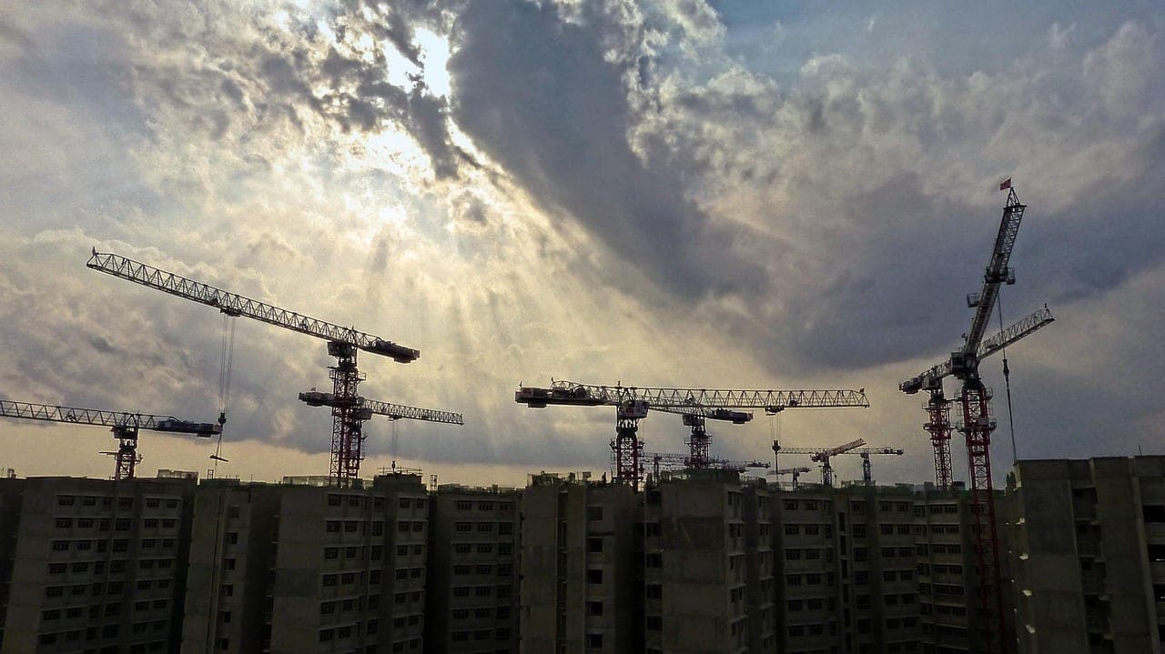 Tower cranes above unfinished high-rise buildings, backlit.