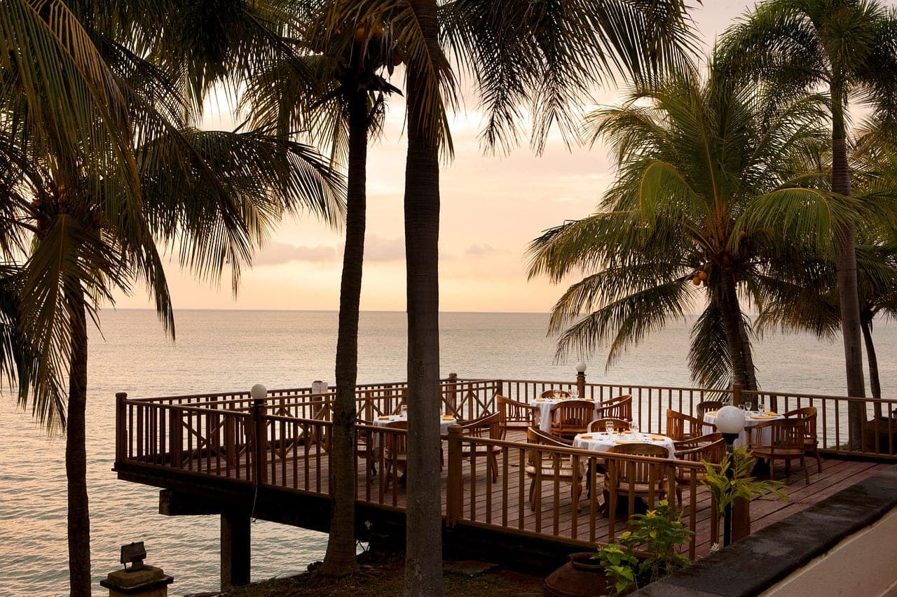 A wooden deck built out over the water, tables set facing the sunset.