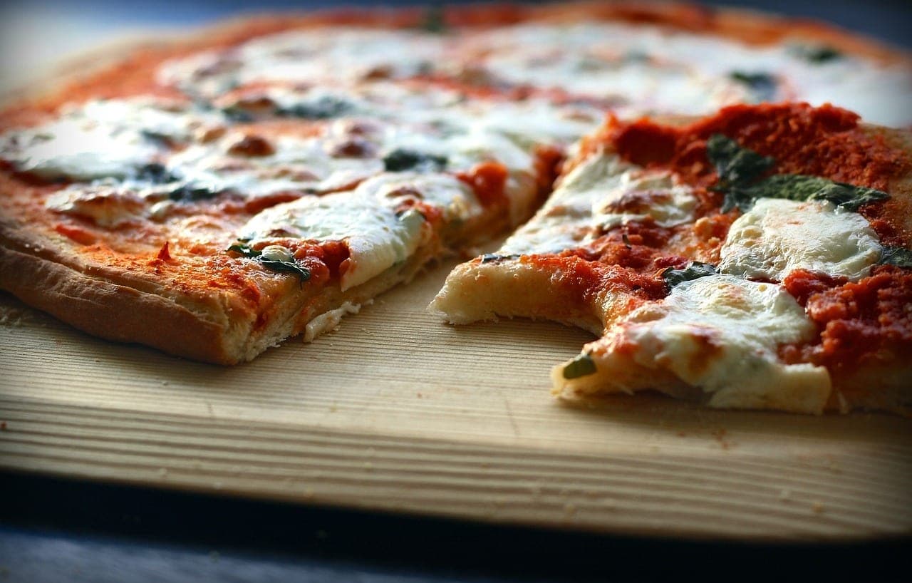 A tomato, mozzarella and basil pizza on a wooden board, one slice pulled away.