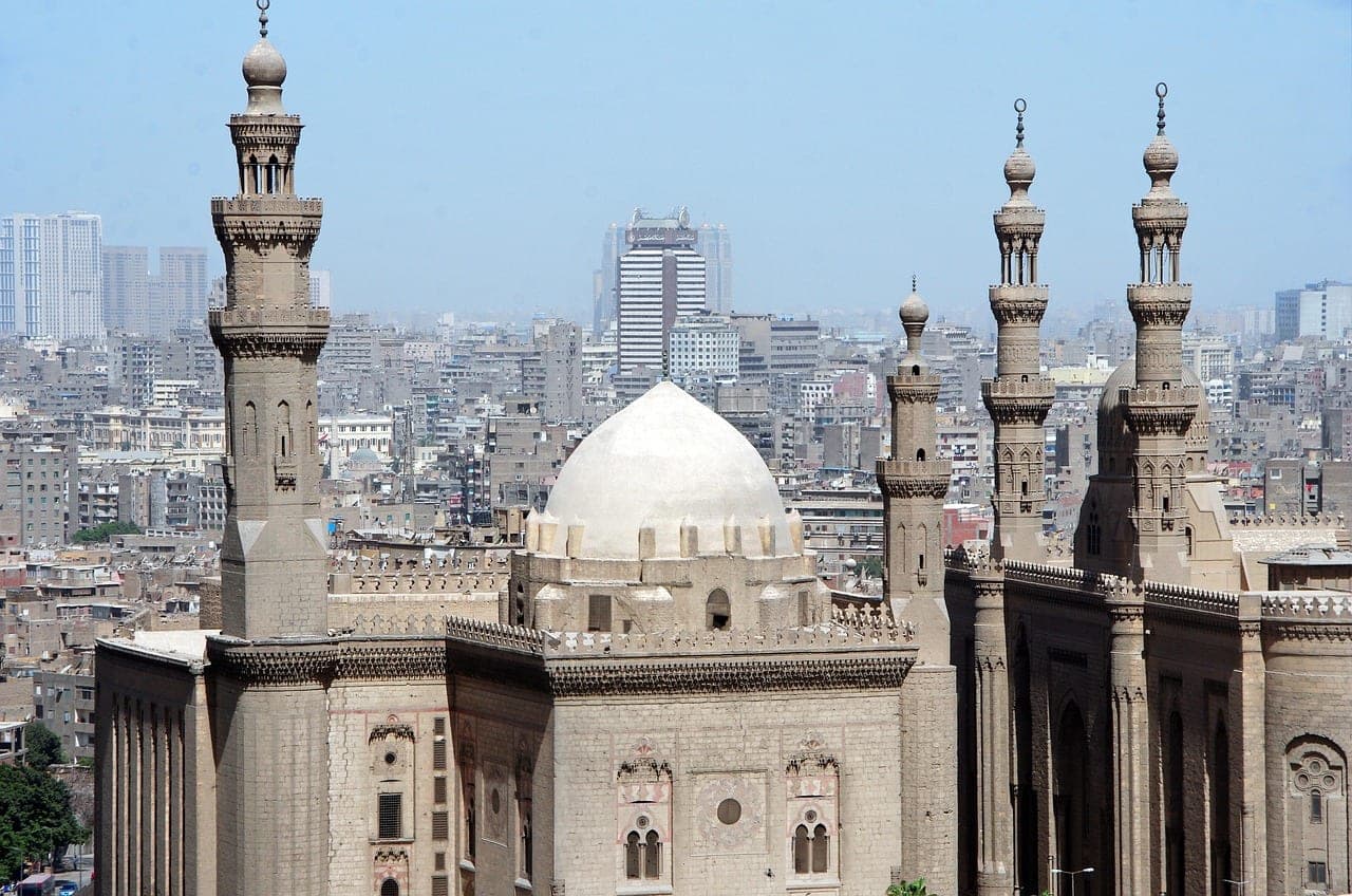 A white dome and stone minarets of Islamic Cairo, above the city's rooftops.