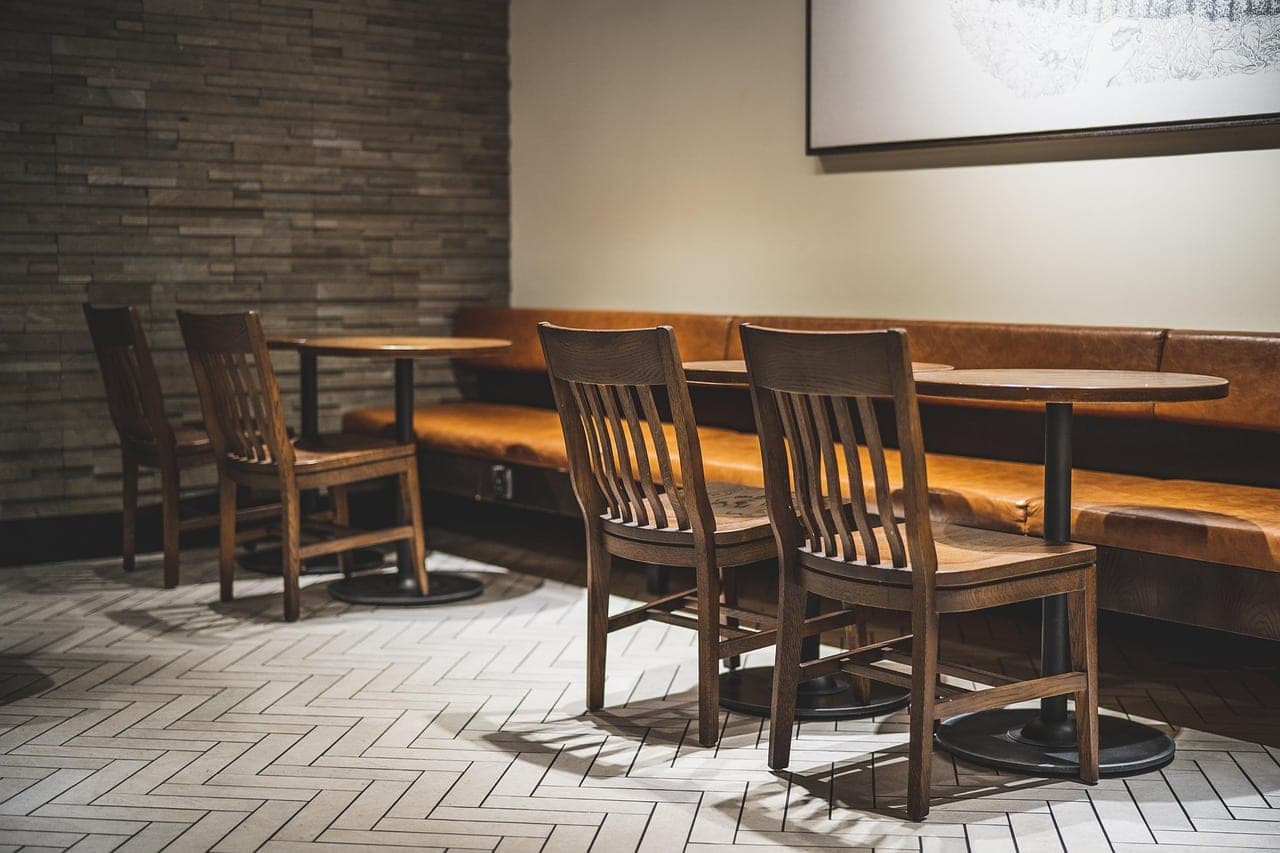 An empty cafe room: a leather banquette, round tables and wooden chairs.