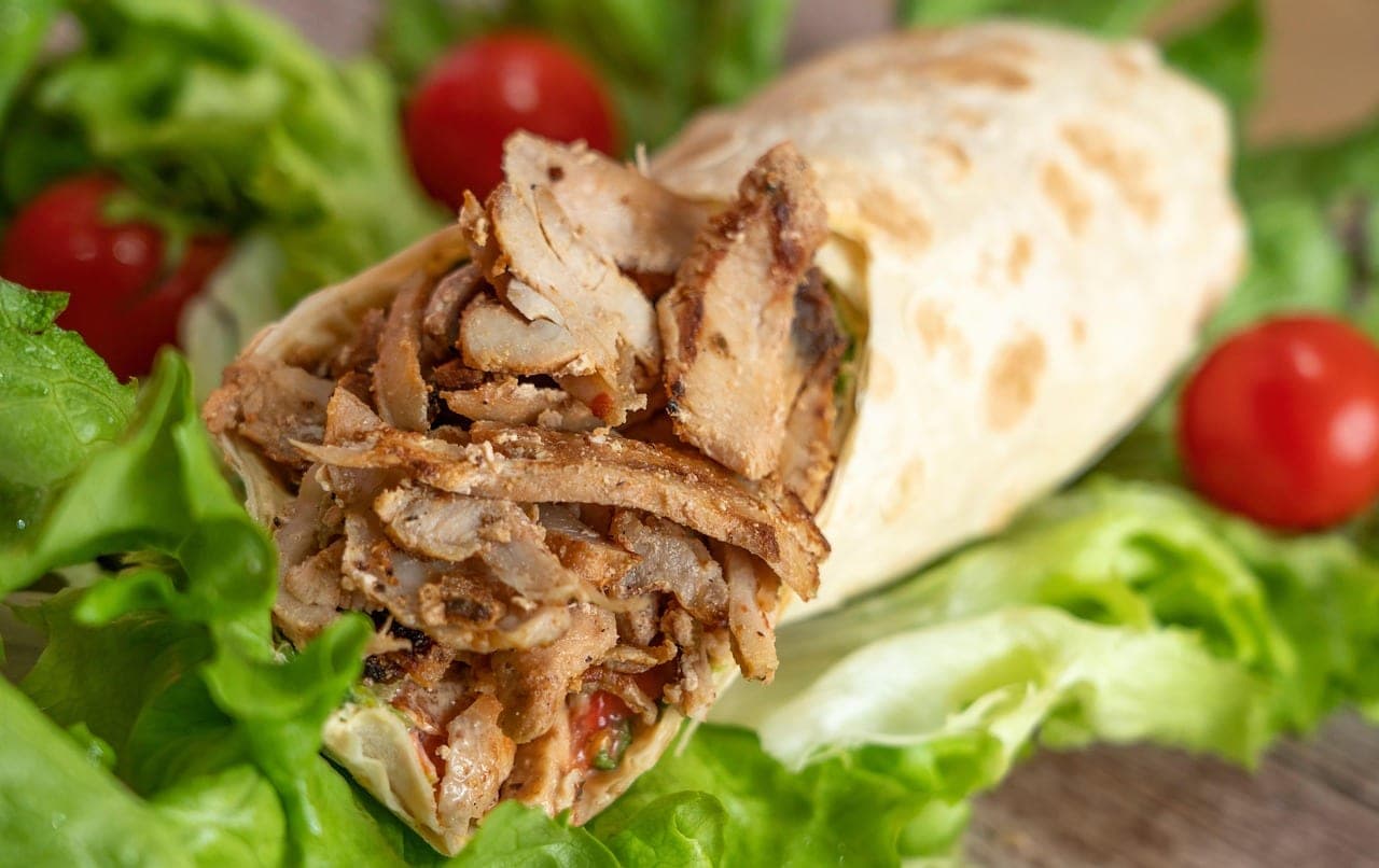Thinly sliced grilled meat rolled in flatbread, set on lettuce.