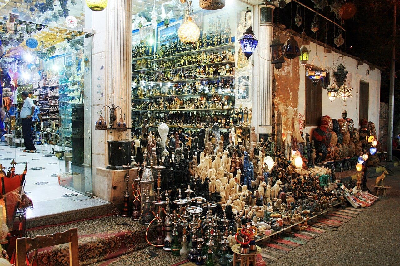 A bazaar stall lit at night, hanging lanterns and rows of alabaster figurines spilling onto the pavement.