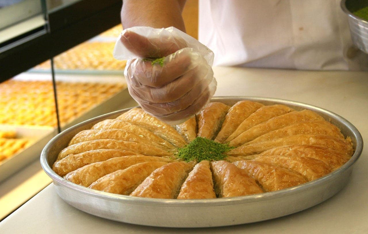 A large tray of baklava being dusted with ground pistachio at the counter.