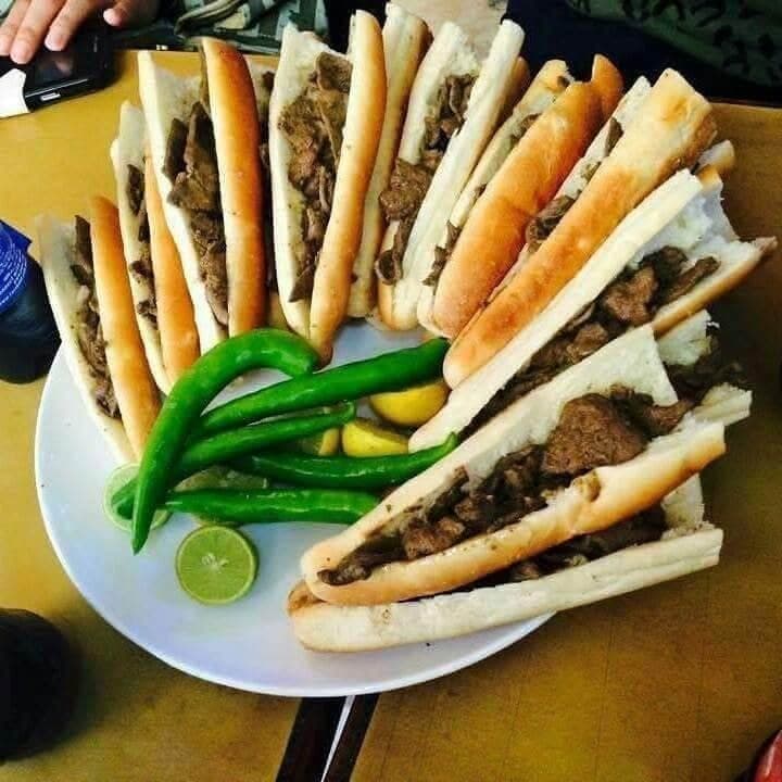 A platter of liver sandwiches in flatbread, with green chillies and lemon halves.
