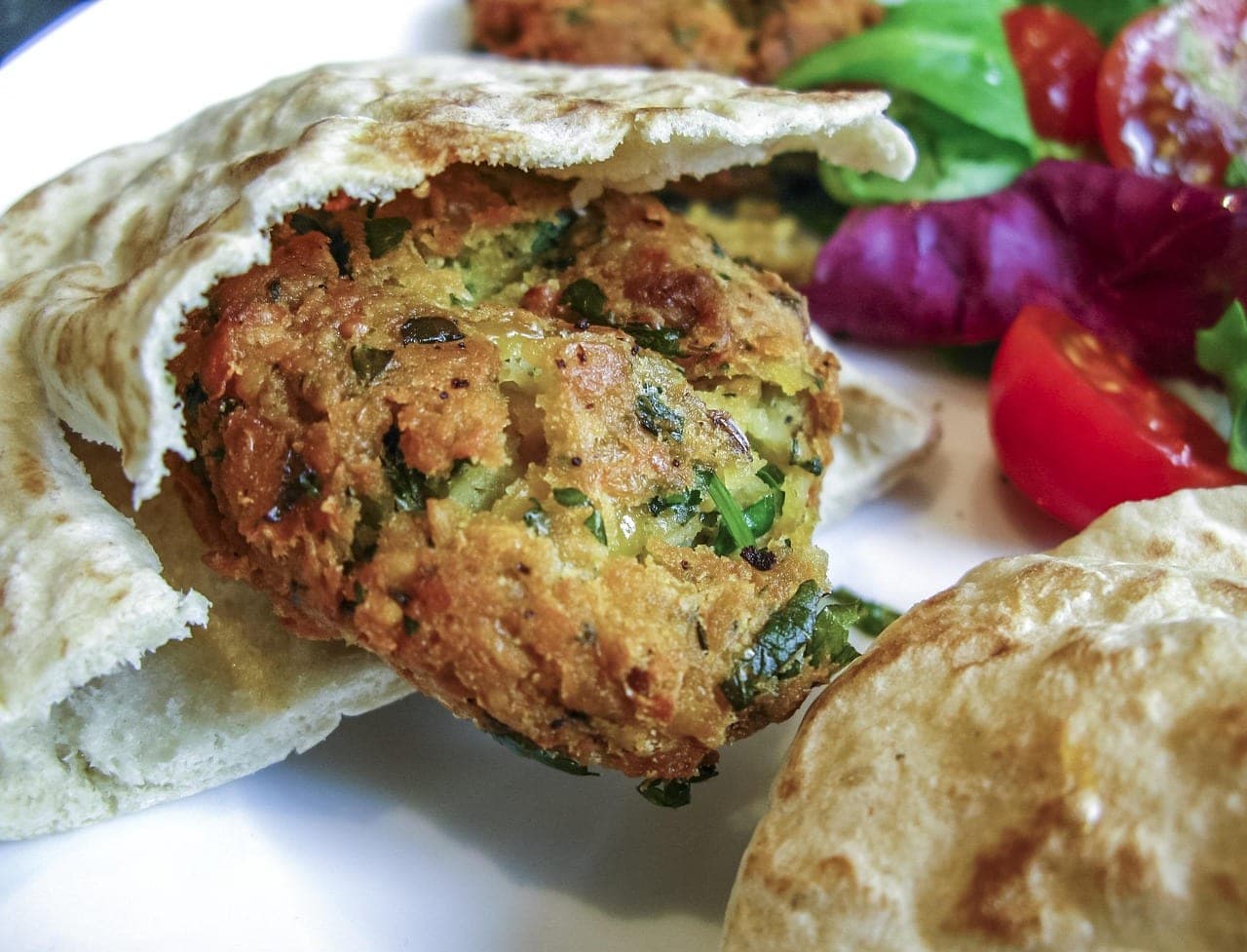 A golden falafel patty flecked with herbs, tucked into flatbread.