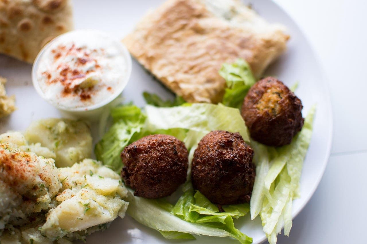 Falafel balls on lettuce, a bowl of white cream dusted with paprika and flatbread, all on one plate.