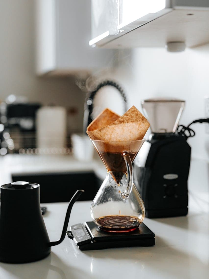 A pour-over coffee being brewed: glass carafe, scale and grinder.