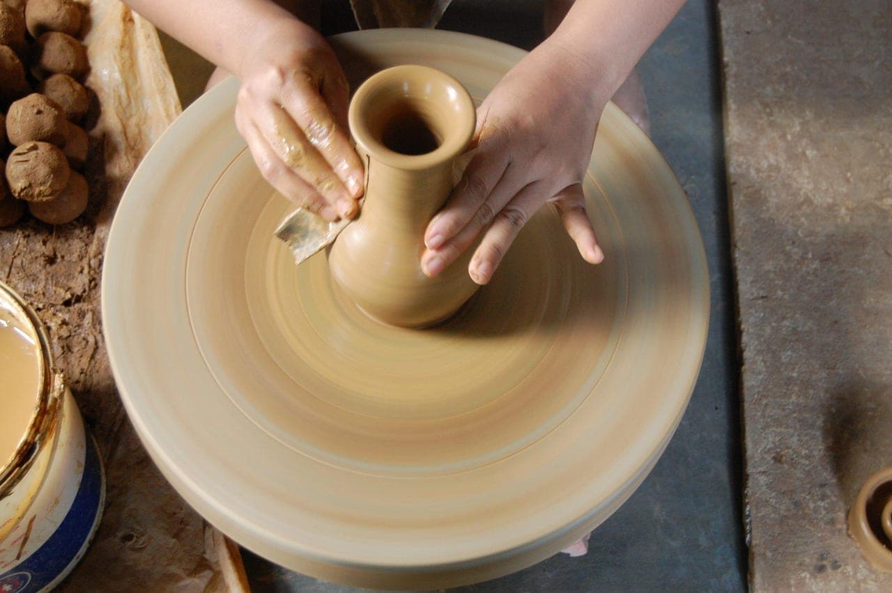 Two hands shaping a small jug on a turning potter's wheel.