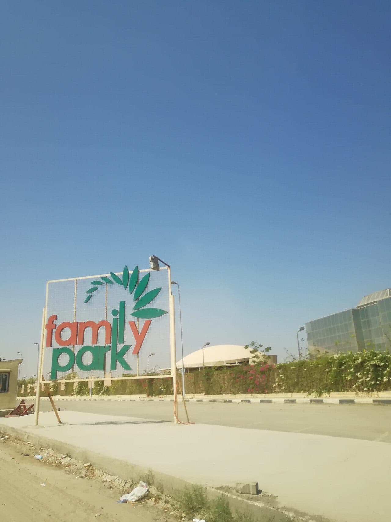 The large “family park” sign by the road, with a white dome behind the flowering hedge.