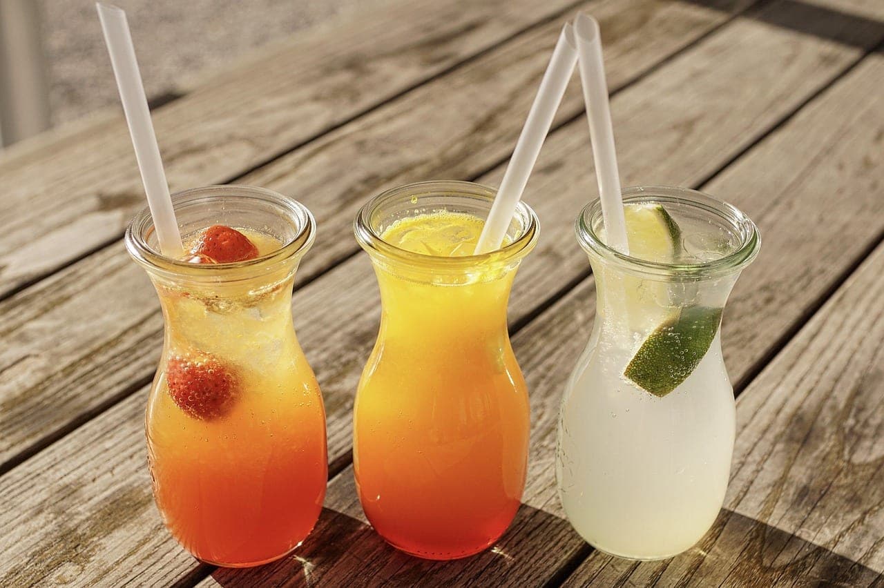 Three glasses of fruit juice — strawberry, orange, lime — on a wooden table.