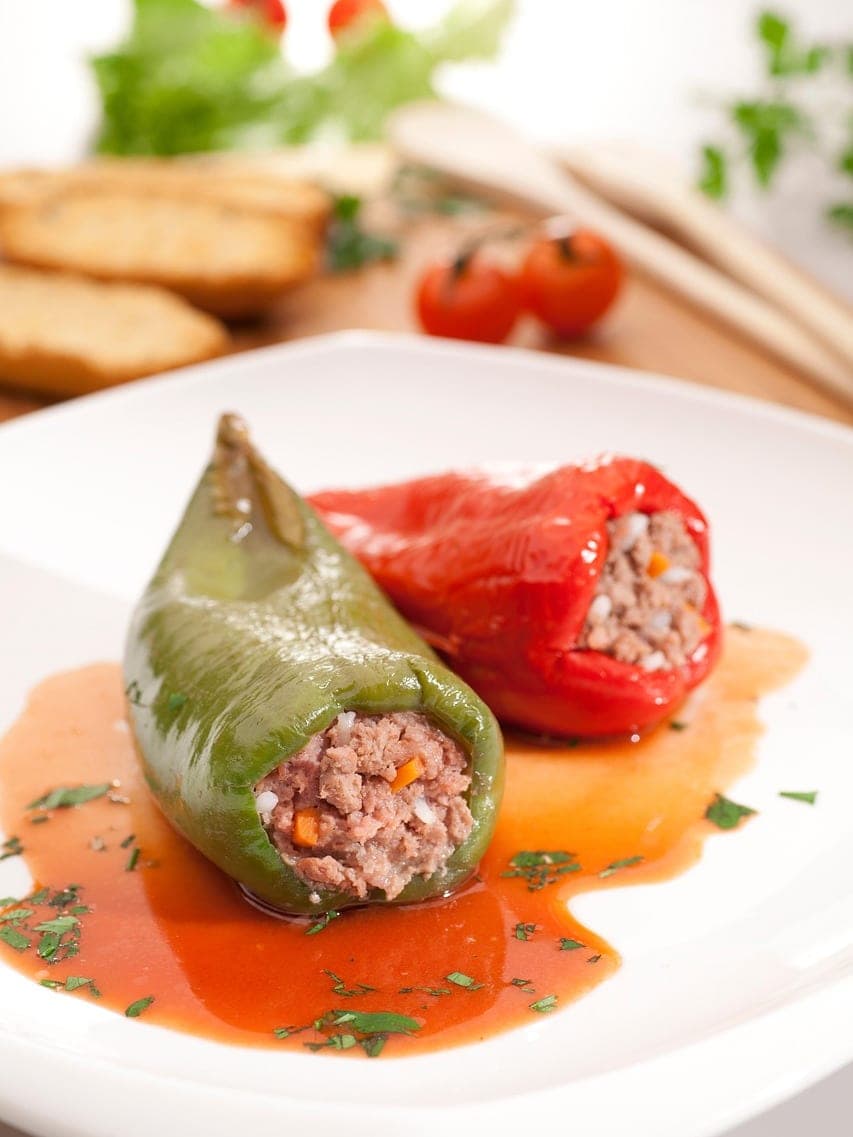 Two peppers stuffed with minced meat in tomato sauce on a white plate.