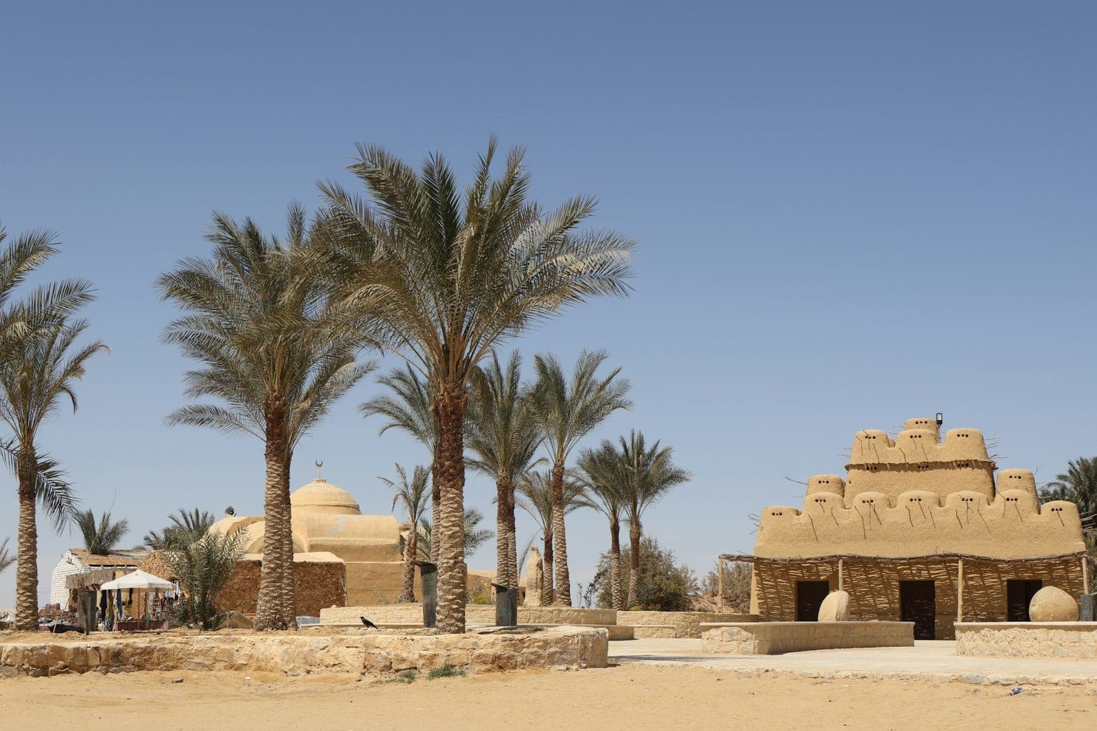A mud-brick lodge, domes and palms, at the desert's edge.