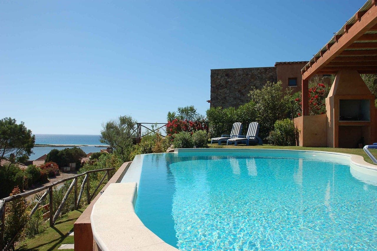 An infinity pool at the edge of a garden, two empty loungers and the blue sea on the horizon.