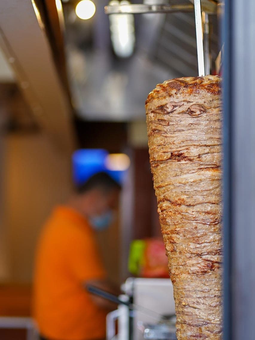 A shawarma spit turning in front of a shop counter.