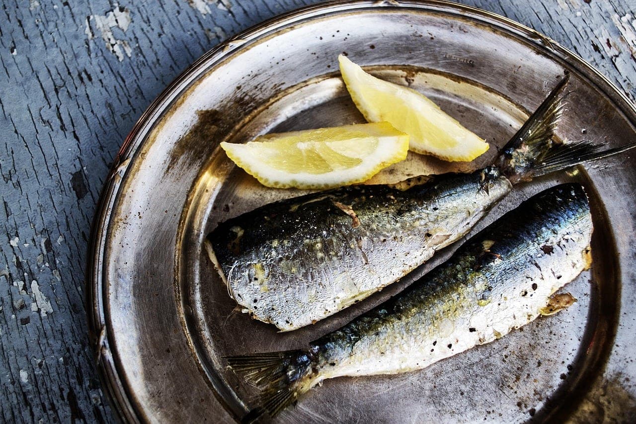 Two whole grilled fish with lemon wedges on a metal plate.