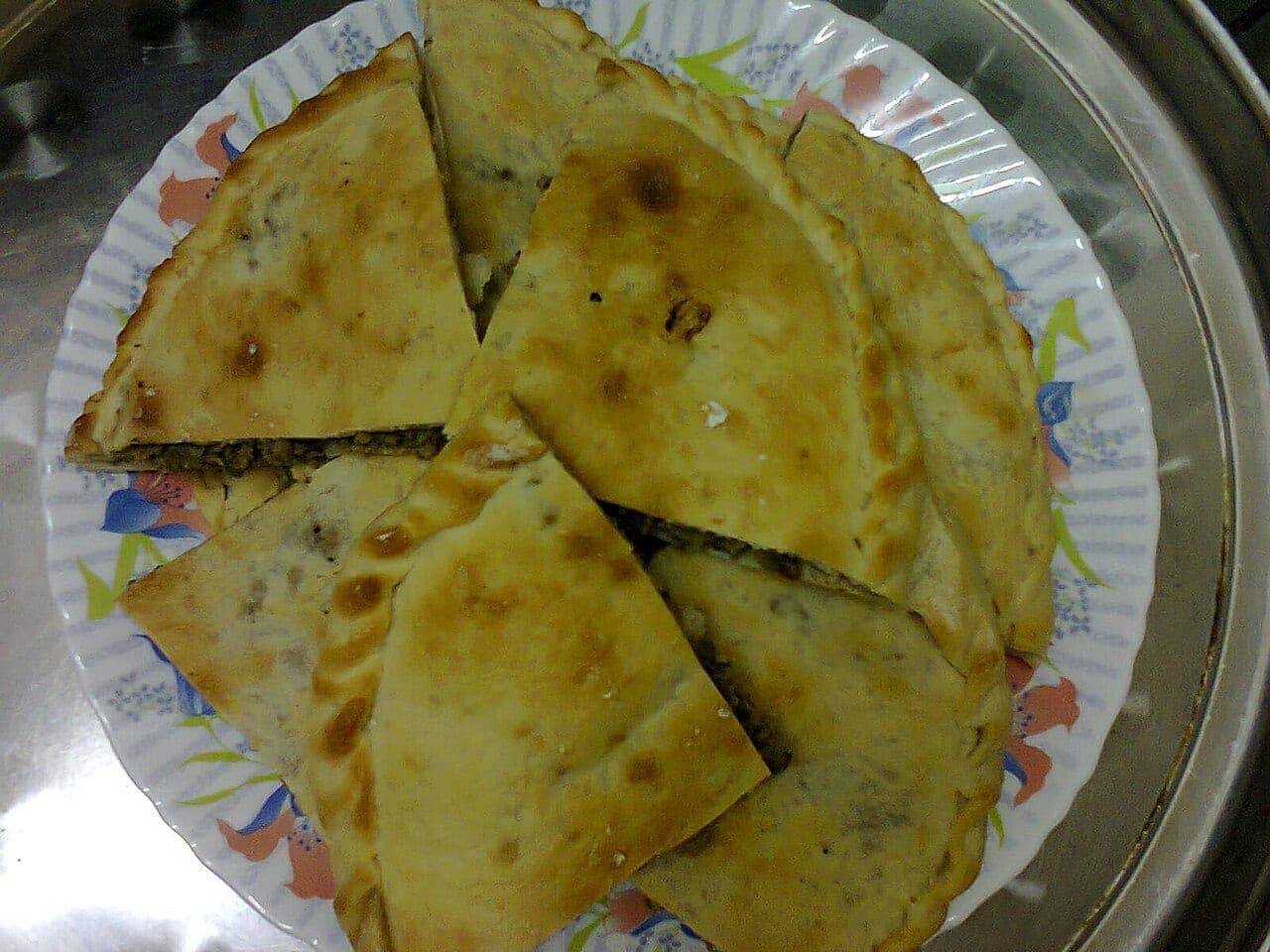 A flatbread stuffed with minced meat, oven-browned and cut into wedges on a plate.