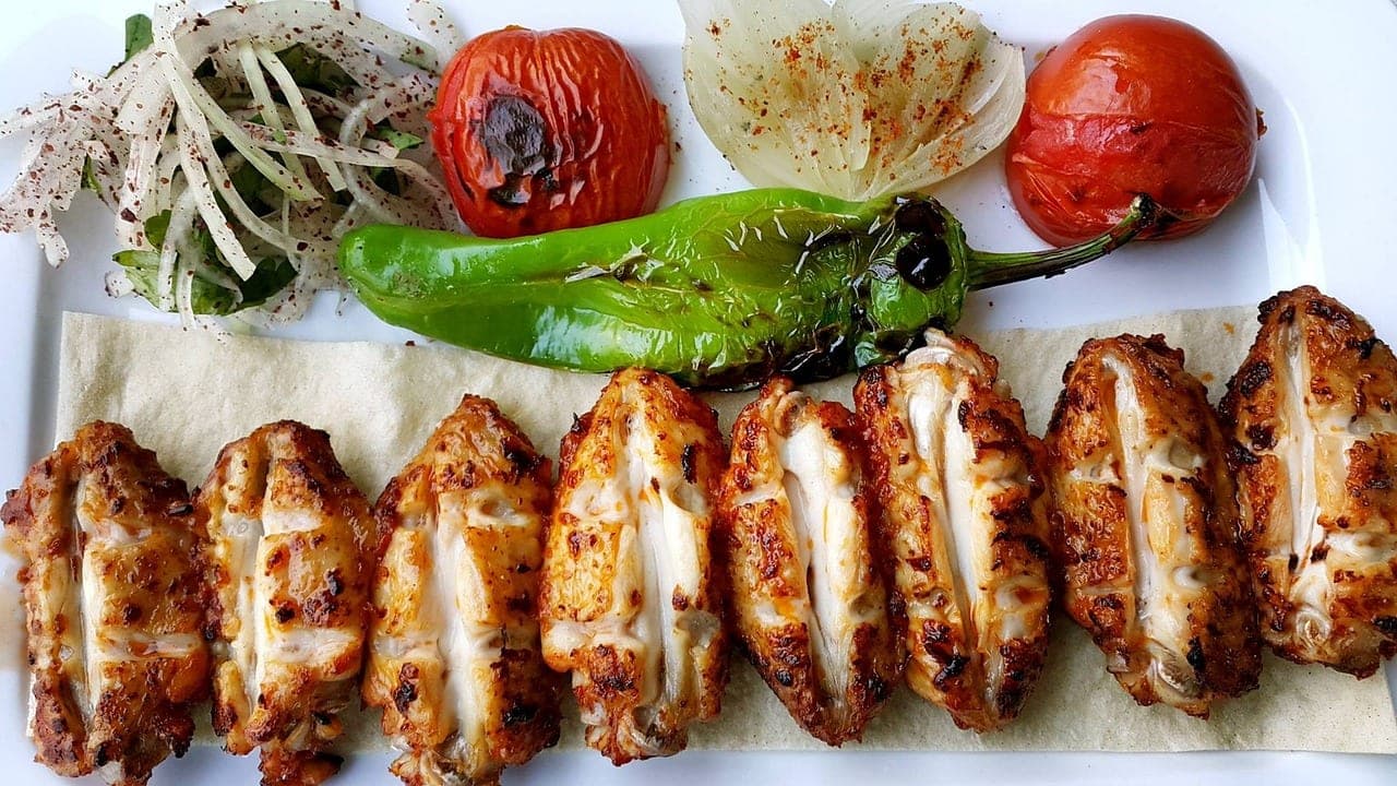Grilled chicken pieces lined up on flatbread with charred pepper, tomato and onion.