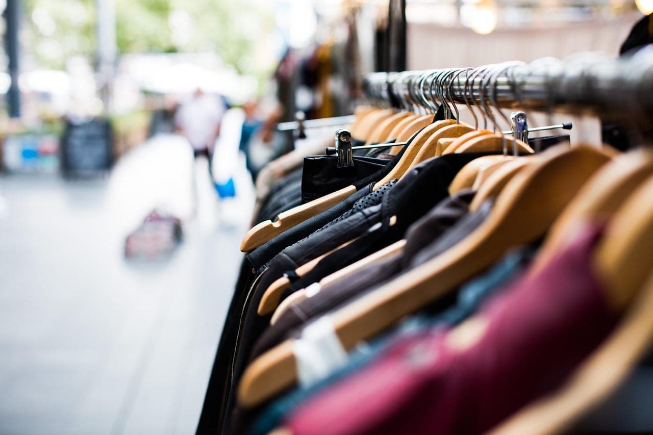 Clothes on wooden hangers, lined up on a rail.