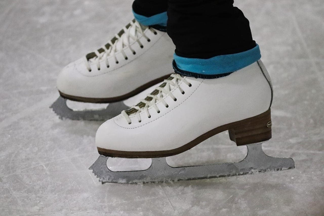 A pair of white figure skates, blades resting on scored ice.