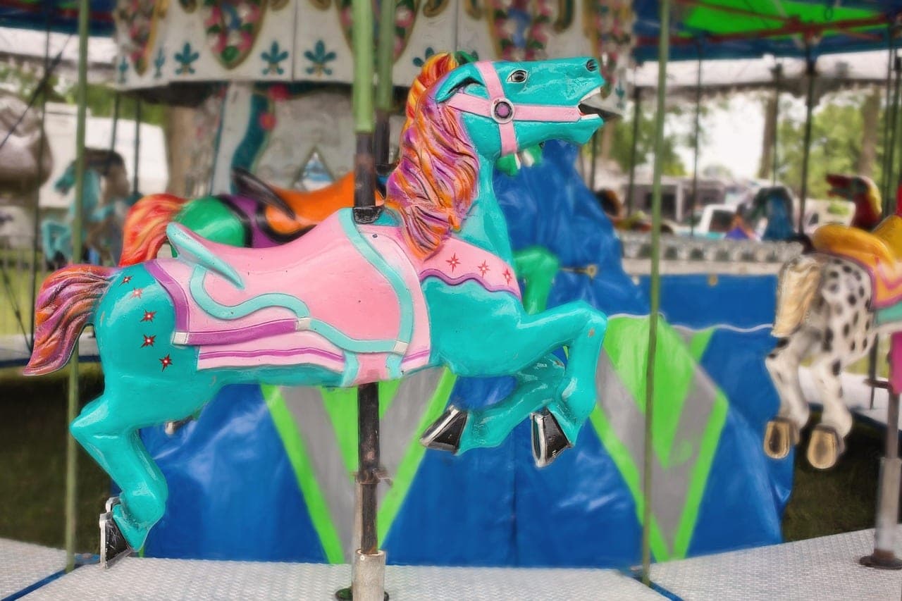 A carousel horse painted turquoise and pink, under the canopy of a merry-go-round.
