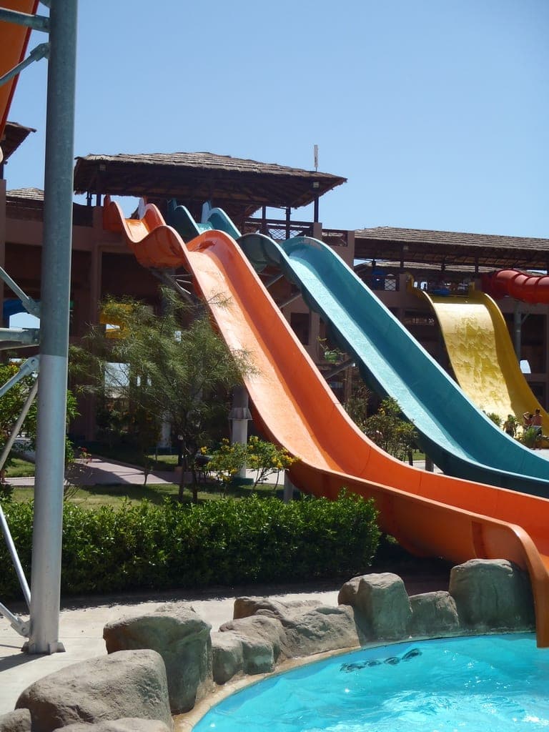 Four coloured slides running down to a pool, under thatched roofs.