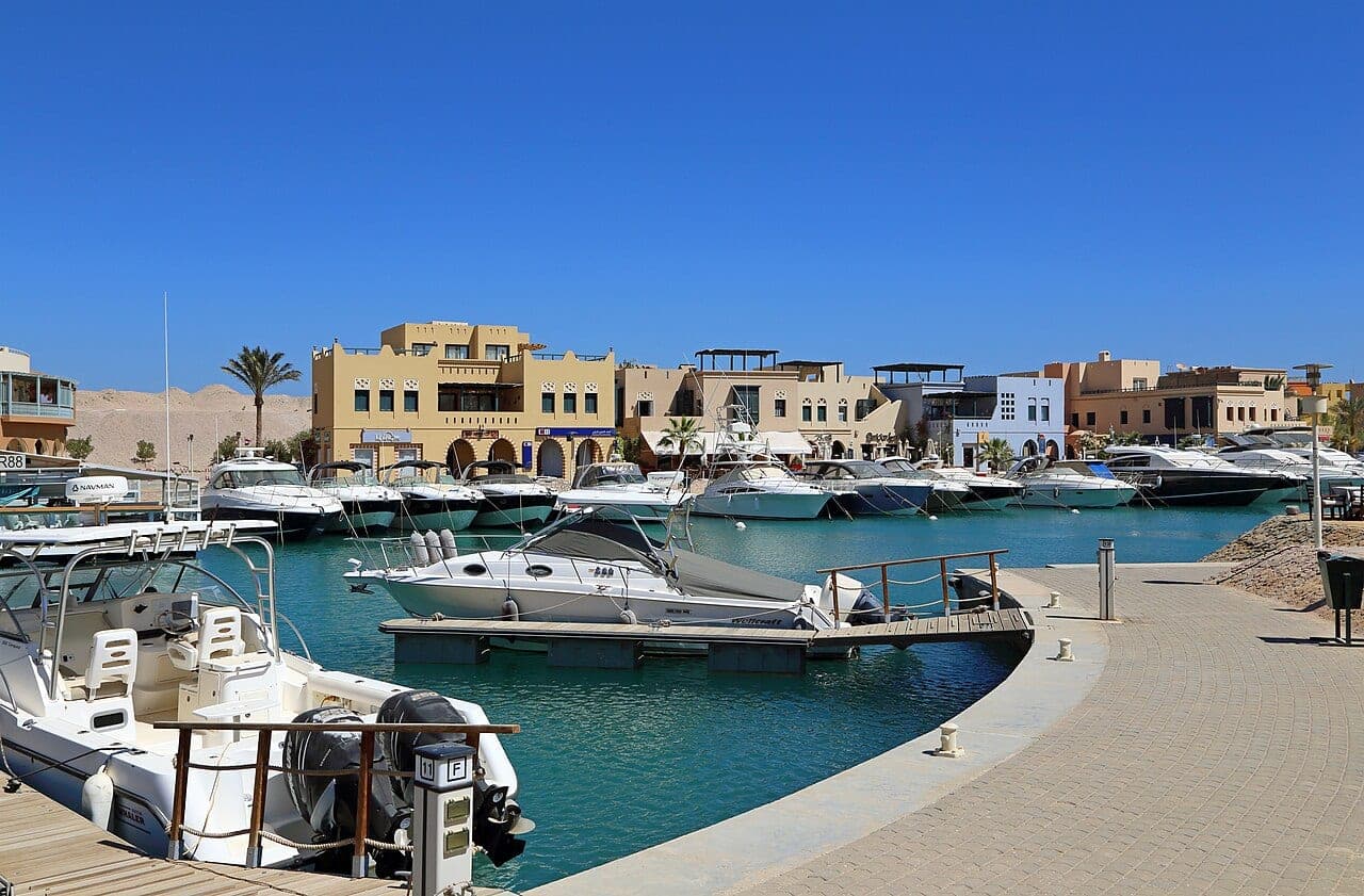 The marina pontoons, boats moored in front of ochre houses.