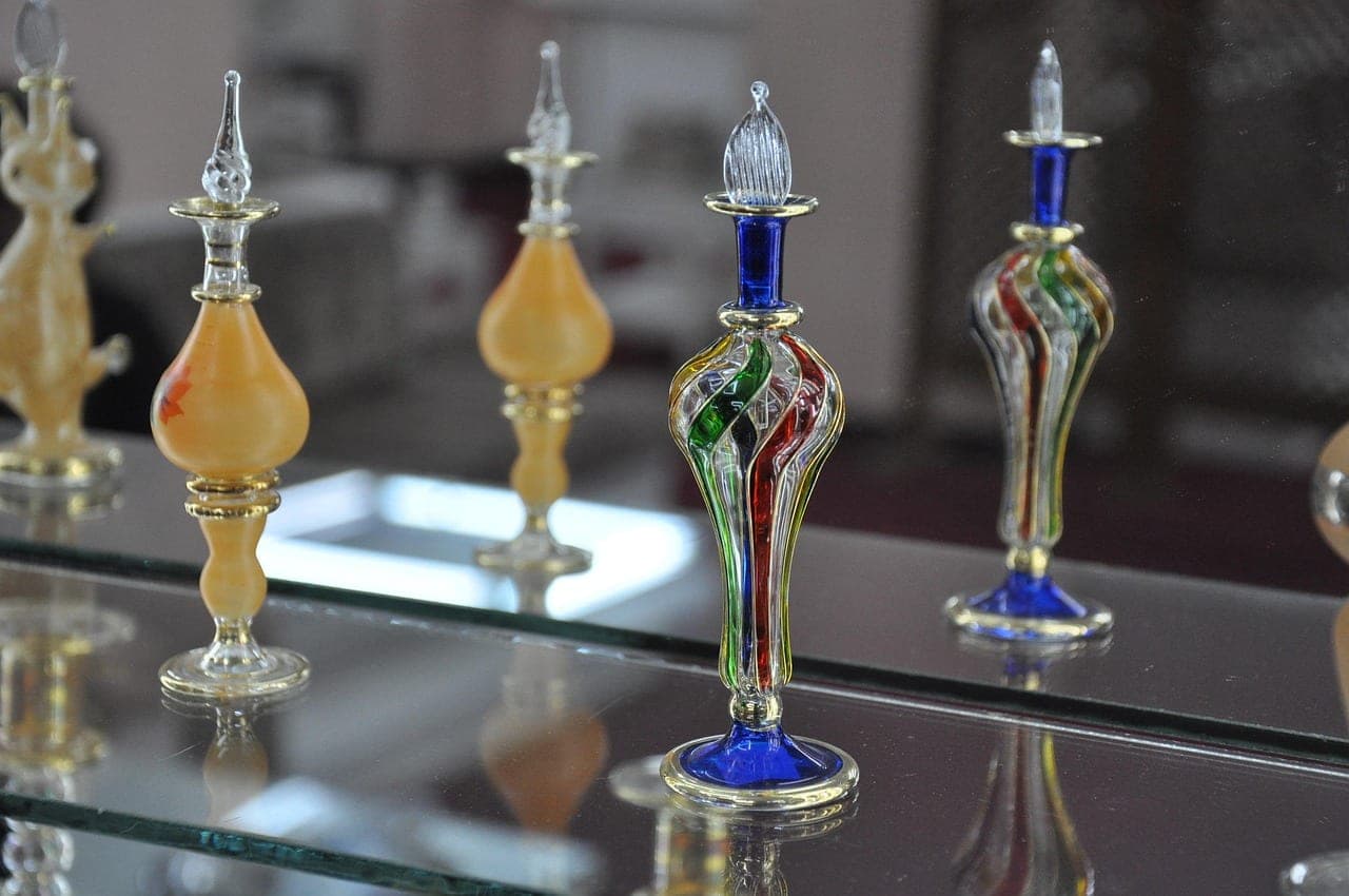 Hand-blown glass perfume bottles, twisted with colour, set on a glass shelf.