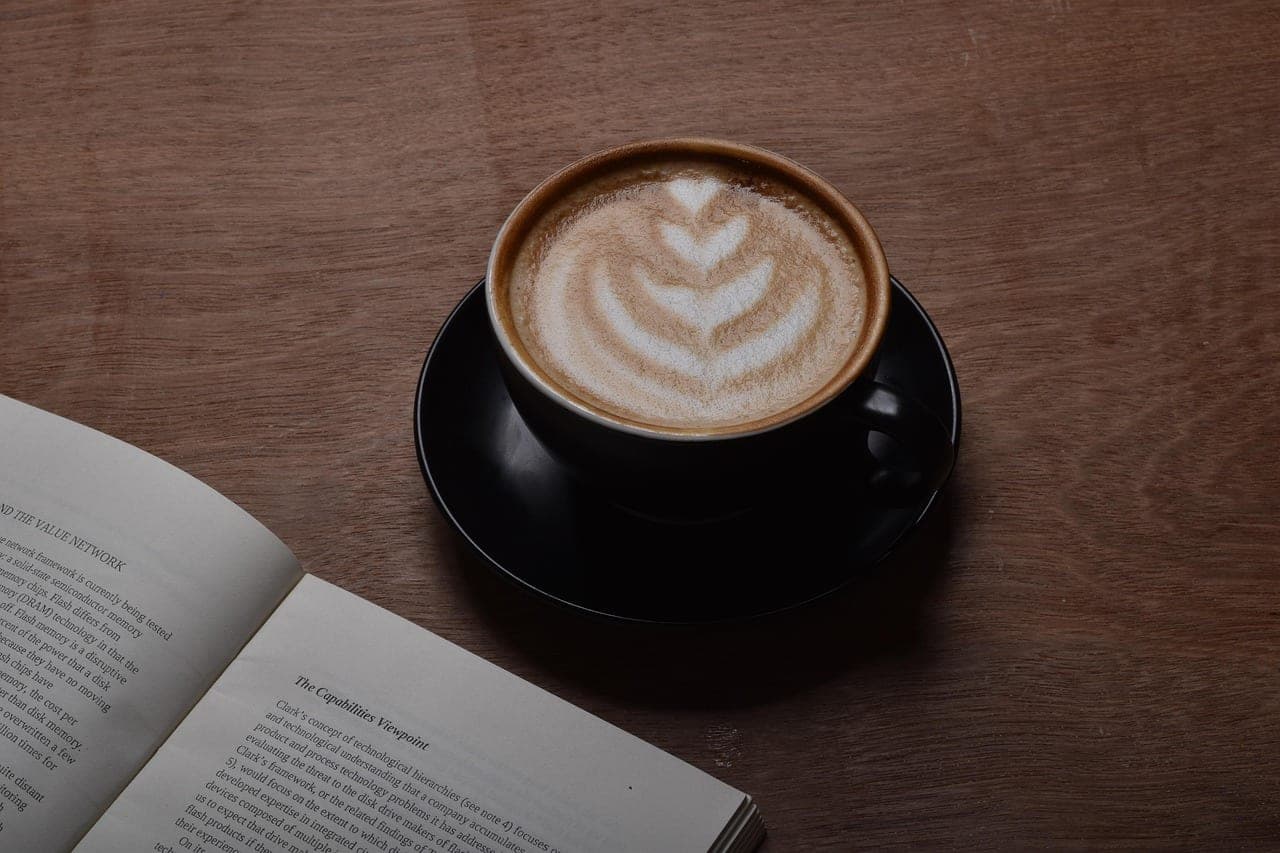 A cappuccino on a wooden table, next to an open book.