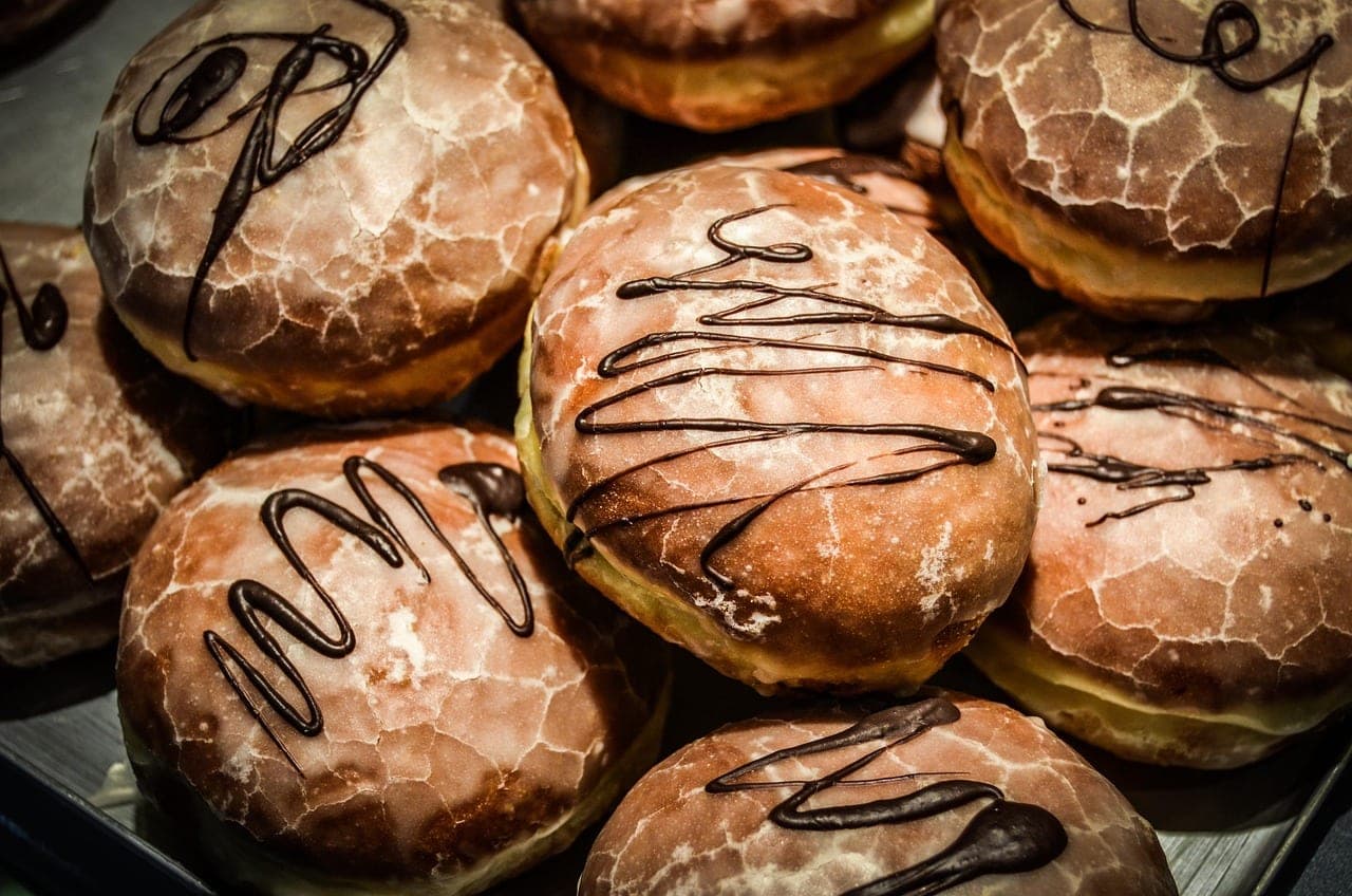 Glazed doughnuts drizzled with chocolate, piled on a tray.