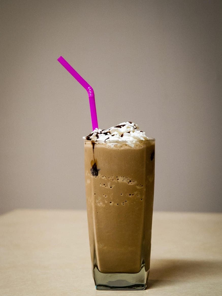 A milkshake in a tall glass, with whipped cream, chocolate sauce and a pink straw.