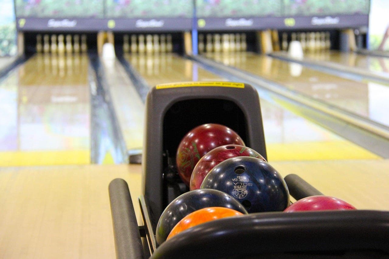 Coloured bowling balls on the ball return, in front of the lanes and the pins.