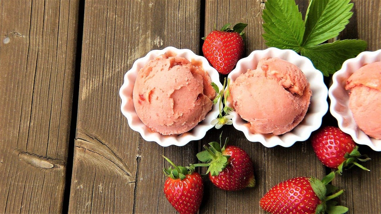 Scoops of strawberry ice cream in white dishes, surrounded by fresh strawberries.