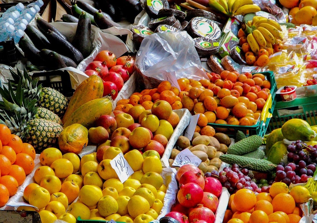 A fruit stall loaded to the edge: pineapples, papayas, pomegranates, oranges and bananas, prices handwritten on scraps of paper.