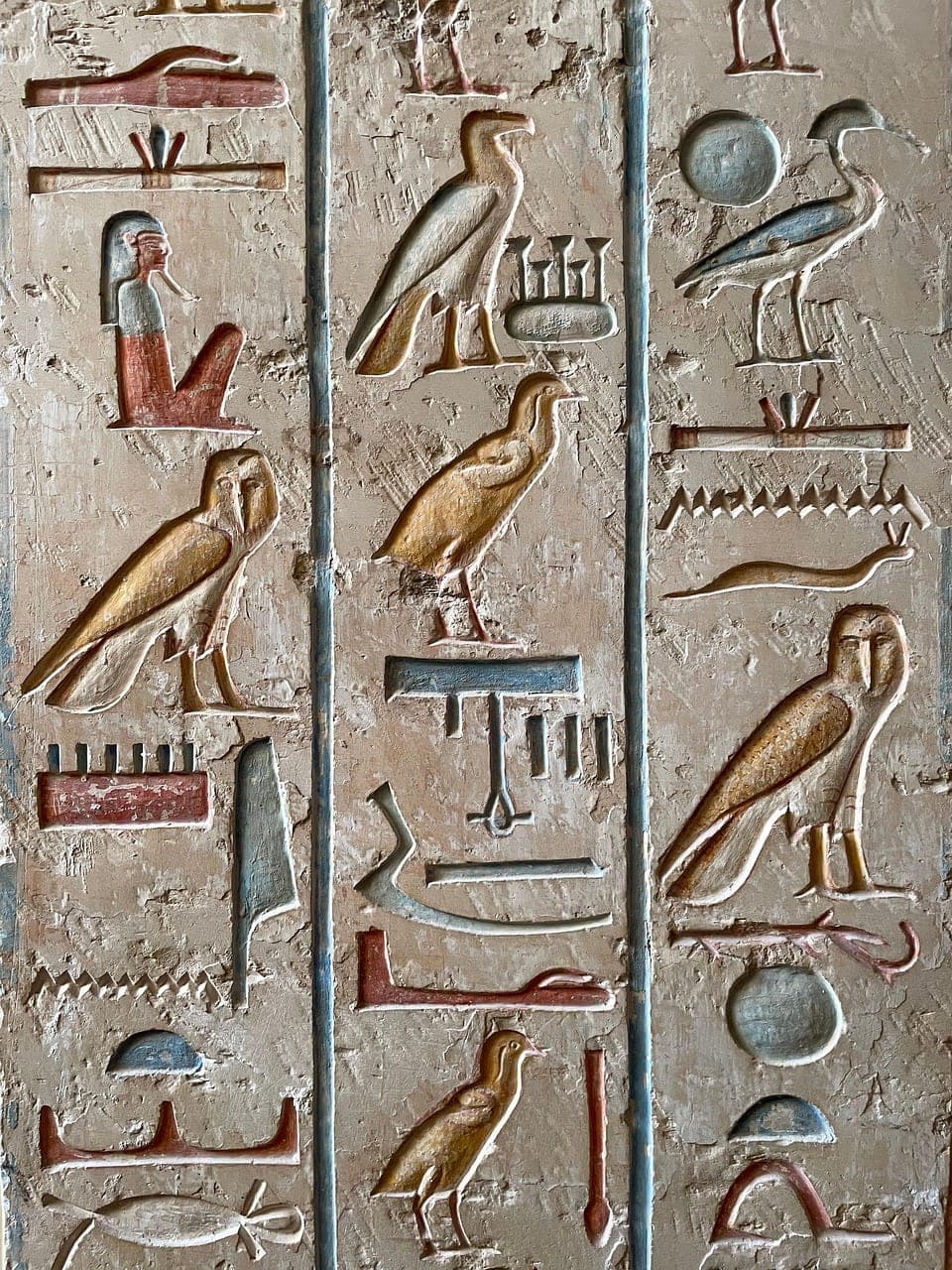 Carved hieroglyphs, painted in ochre and blue, on the wall of an ancient Egyptian temple.
