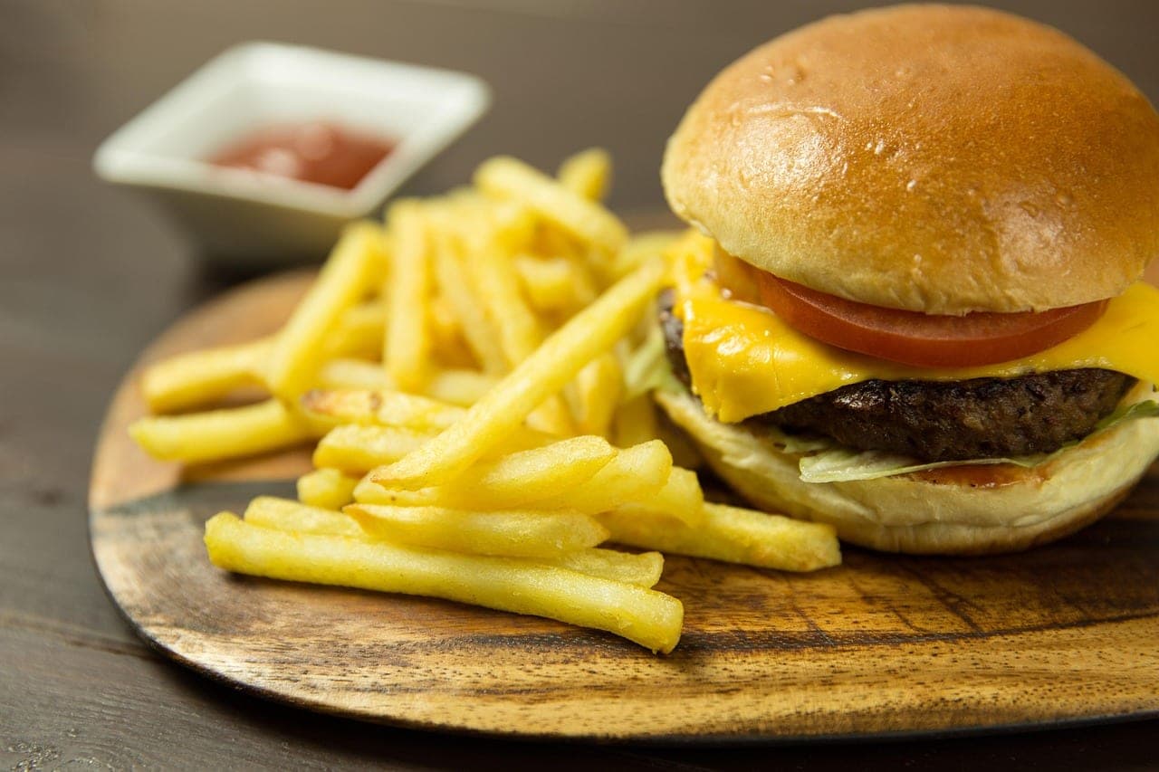 A cheeseburger and fries on a wooden board, with a small dish of ketchup.