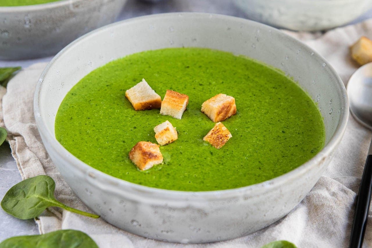 A thick green soup in a bowl, topped with a few golden croutons.